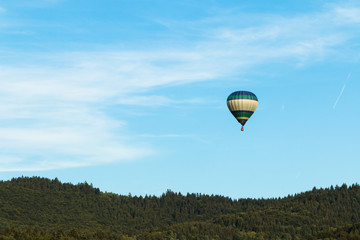 colorful hot air balloon flying on blue sky over green hills 
