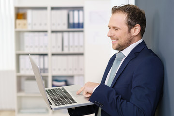 geschäftsmann steht im büro und schaut auf sein notebook