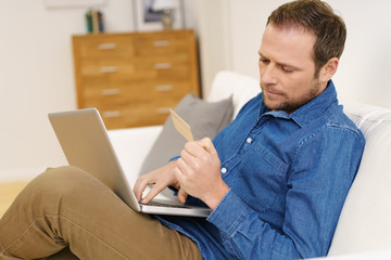 mann sitzt auf dem sofa mit laptop und kreditkarte