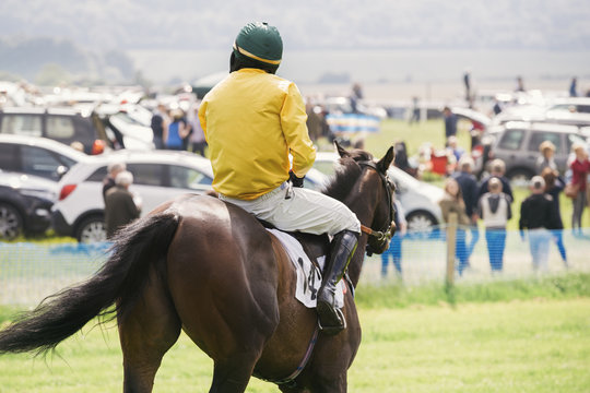 Rear view of a jockey in a yellow vest riding a race horse.