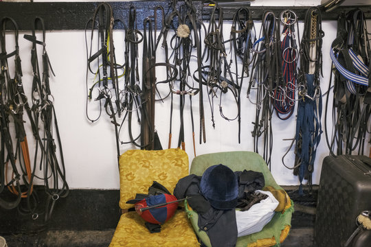 Riding tack on hooks and riding gear on an old armchair in a stable.
