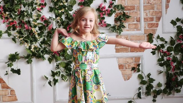 little blond girl in a green dress barefoot having fun, dancing, in studio, slow motion, close up