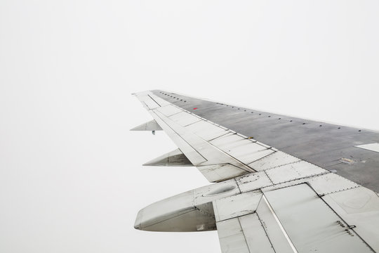 An aeroplane wing in flight against a grey cloudy sky.