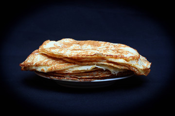 Russian pancakes on a plate against dark background