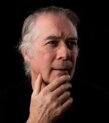  close up portrait headshot of a senior man in his 50's. male wearing black t-shirt and isolated oin black background.