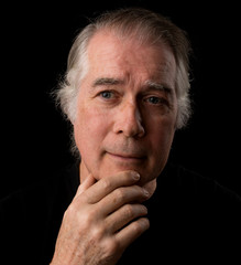  close up portrait headshot of a senior man in his 50's. male wearing black t-shirt and isolated oin black background.