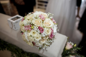 Bouquet composto da tanti fiori di vari colori sopra sopra banchetto della messa e sullo sfondo gli sposi sfocati