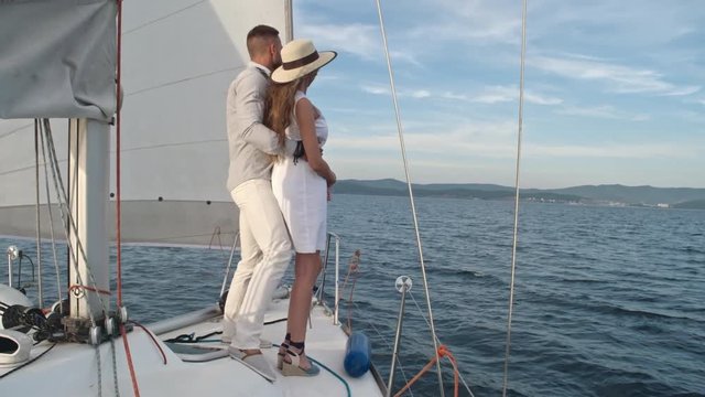 Rear view of loving couple standing on yacht and embracing while sailing on beautiful lake in summer