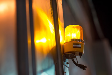 Close-up detail of a yellow revolving warning light shining onto a metal wall at a construction site. Industry and construction concept. - obrazy, fototapety, plakaty