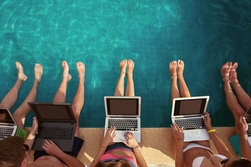 Group of people freelancers using laptop computer sitting near swimming pool and work together
