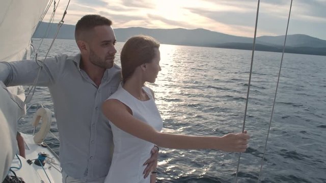 Romantic couple embracing on yacht drifting along lake coast at sunset 