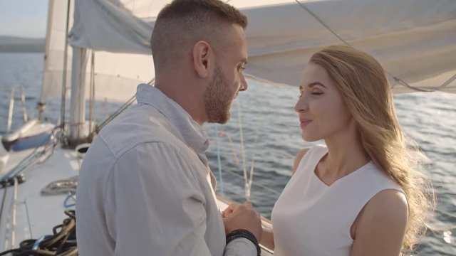 Happy young woman listening to her boyfriend holding her hand and telling something on drifting yacht
