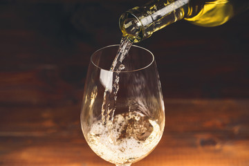 Pouring white wine from a bottle in a wineglasses on wooden background. Free space