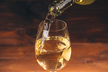 Pouring white wine from a bottle in a wineglasses on wooden background. Free space