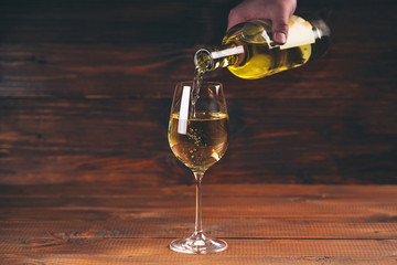 Pouring white wine from a bottle in a close up view of the wineglasses against wooden background
