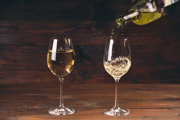 Two glasses pouring white wine from a bottle in a wineglass on wooden background