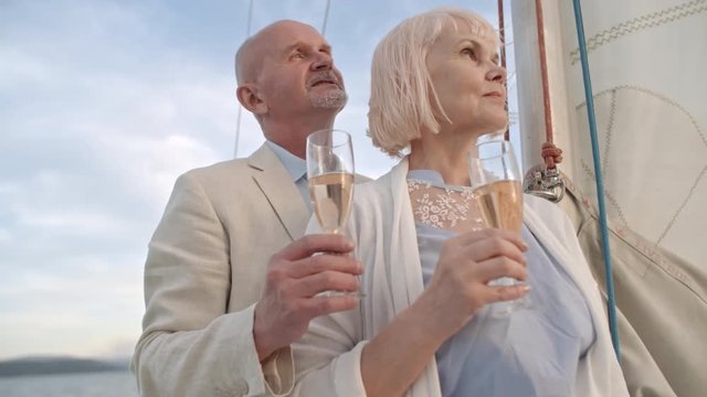 Senior man standing with wife with champagne flutes on drifting yacht