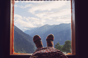 Legs of traveler in Warm socks near window with Himalaya Mountains view. Freedom concept, relax and enjoy mountain from indoor
