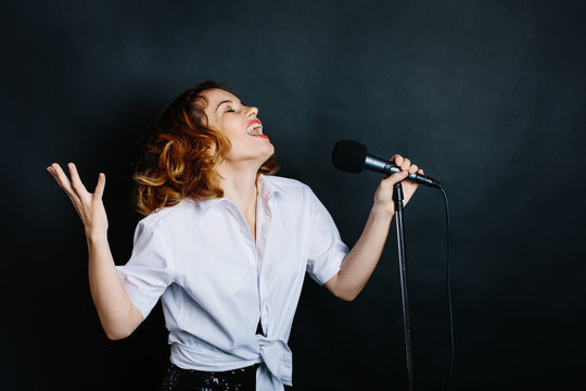 portrait of woman singer with microphone in dark studio background