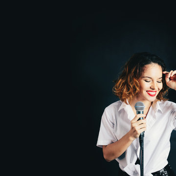 Studio portrait of woman singer with microphone in dark background