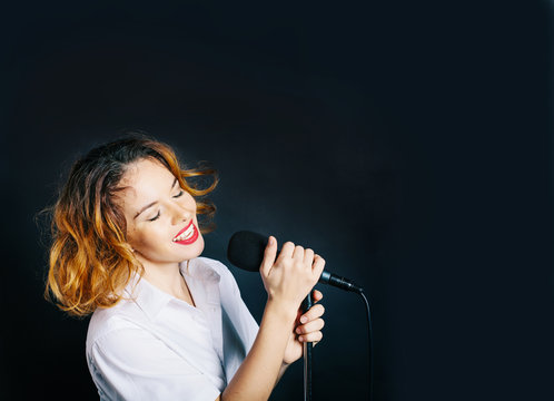 portrait of woman singer with microphone in dark studio background