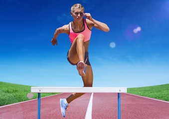 Female athlete jumping over hurdle on race track - Powered by Adobe
