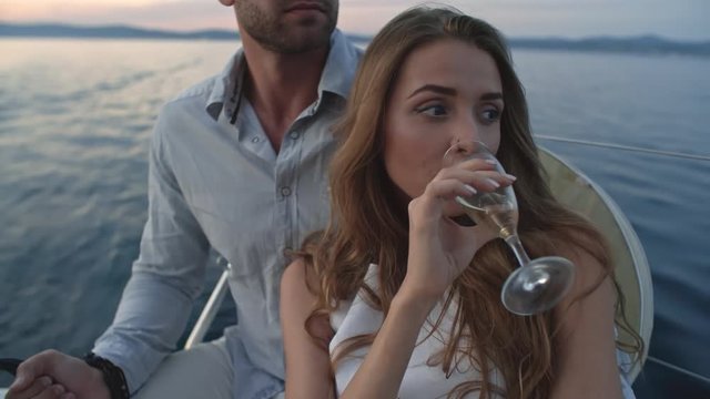 Closeup of pretty young lady enjoying glass of white wine while sitting with her boyfriend on yacht