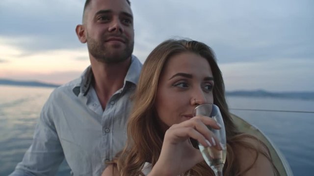 Closeup of pretty young lady sipping wine while embracing with her boyfriend on yacht in the evening