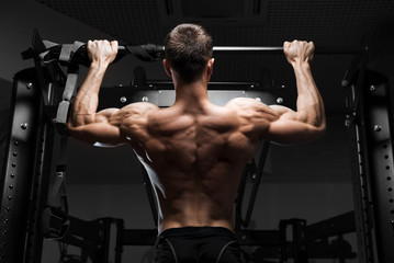 Obraz na płótnie Canvas Athlete muscular fitness male model pulling up on horizontal bar