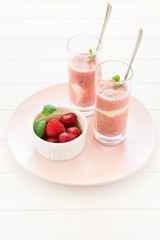 Two glasses with fresh strawberry and banana smoothie decorated mint leaves on white wooden background. Selective focus