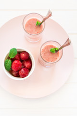 Two glasses with fresh strawberry and banana smoothie decorated mint leaves on white wooden background. Selective focus