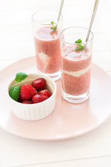 Two glasses with fresh strawberry and banana smoothie decorated mint leaves on white wooden background. Selective focus
