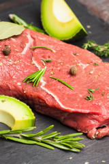 Fresh raw beef meat with avocado and herbs on the black stone background
