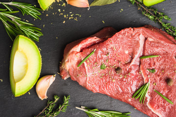 Fresh raw beef meat with avocado and herbs on the black stone background