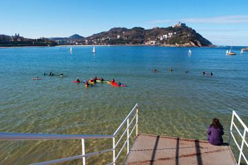 Donostia-San Sebastian, Paesi Baschi, Spagna, 28/01/2017: una ragazza di spalle seduta sul molo con vista sulla spiaggia di La Concha, vista panoramica