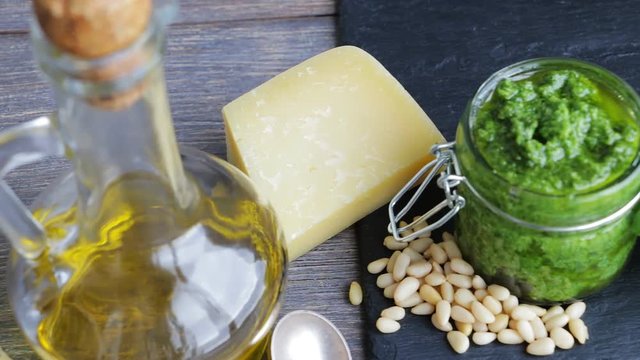 Ingredients for pesto sauce and pesto sauce in glass jar - italian cuisine - olive oil, basil herbs, cedar nuts, parmesan cheese and garlic - on wooden table with mortar