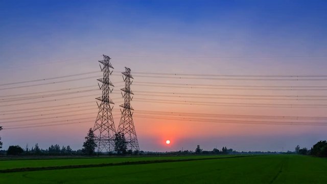 4K, Time lapse Electric pole, High voltage towers and sky sunset and green rice field in front as background, day to night, energy power concept.