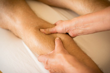 Therapist applying pressure on male leg - hand massage of human calf muscle