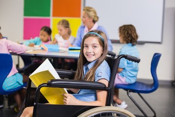 Disabled school girl on wheelchair holding a book in classroom