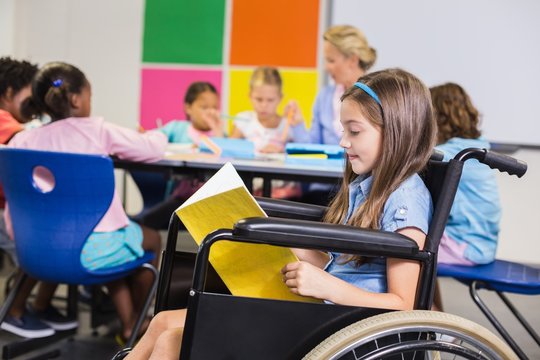 Disabled school girl on wheelchair reading a book in classroom - Powered by Adobe