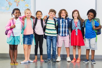 Smiling kids standing with arm around in classroom