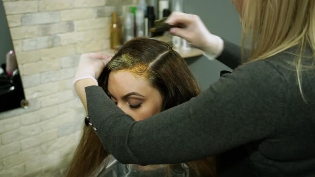 Female blonde barber making hair colouring of young woman at hairdresser's. HD