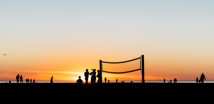People playing volleyball and walking on the beach at Santa Monica, California at sunset.