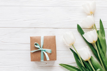 Obraz na płótnie Canvas stylish craft present box and tulips on white wooden rustic background. flat lay with flowers and gift with space for text. hello spring. happy day concept. instagram photo workshop