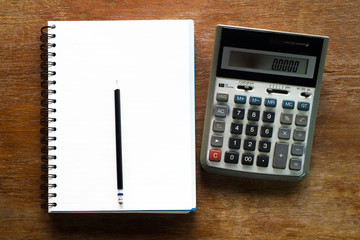 Blank notebook with pencil put on the wooden table close the big calculator 