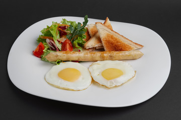 Fried eggs with homemade sausage, toasts and fresh tomato and salad.