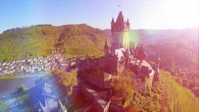Beautiful medieval castle aerial, vine hills, German mid-ages fortress and river, fairy-tale royal castle with vine plants growing on green hills, aerial view with beauty lens flare, sunny day
