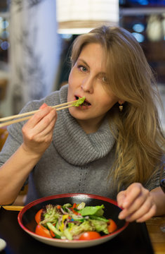 Blonde woman has dinner in japanese restuarant  with sushi and drink red wine
