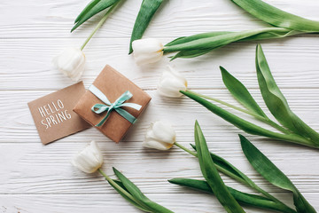 hello spring text sign on stylish craft present box and greeting card and tulips on white wooden rustic background. flat lay with flowers and space for text.