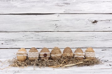 Row of handmade rustic style Easter Eggs in moss against an aged white wood background